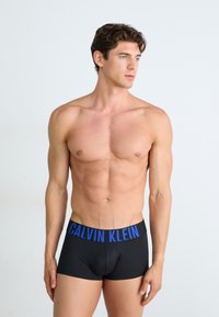 Zwarte boxershorts met een blauw "CALVIN KLEIN" logo op de elastische tailleband. De stof lijkt zacht en rekbaar, en zit nauwsluitend.