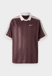 Polo shirt Nike cor vinho com gola e detalhes nas mangas em branco. Apresenta riscas verticais e logótipos repetidos. Tecido leve e suave.