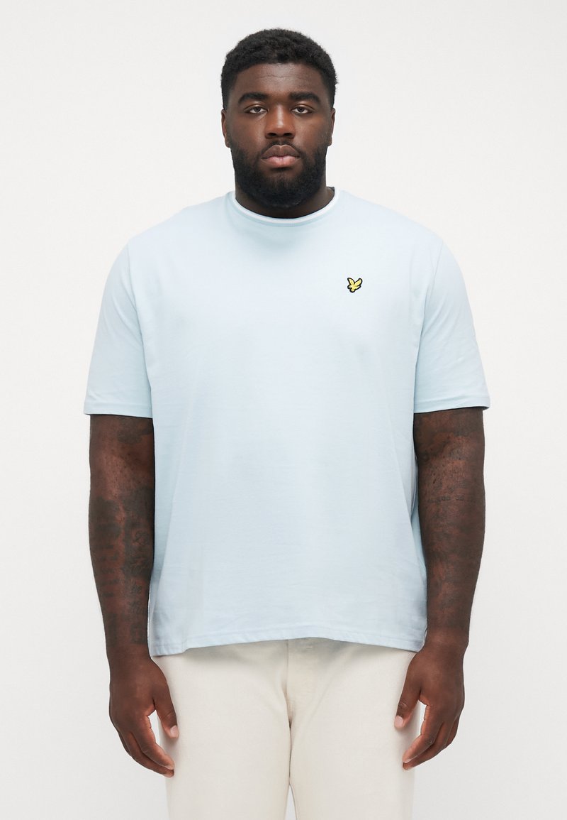 Lyseblå t-shirt lavet af blødt bomuld med rund hals. Har et lille gult sommerfugl-logo på brystet. Enkelt, korte ærmer.