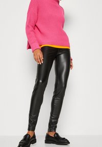 Pink knit turtleneck sweater paired with black faux leather leggings and black loafers. The sweater has a loose fit, ribbed texture, and vibrant color.