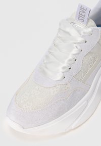 Valged sneakers, millel on nööridega ja võrgust ülemine osa, satiinilaadsed nööbid ning tahke valge tallaga. Ülemises osas on "STEVE" silt.