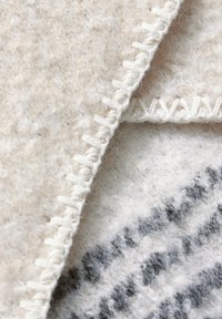 Wollfilzstoff in Creme- und Grautönen, mit sichtbaren Nähten entlang der Kanten und einer strukturierten, leicht flauschigen Oberfläche.