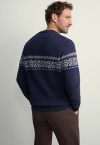 Granatowy sweter z teksturowanym wzorem na plecach, z białymi geometricznymi i kwiatowymi motywami. Ściągacze na mankietach i u dołu.