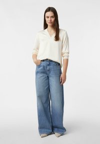 Cremefarbener V-Ausschnitt mit langen Ärmeln, kombiniert mit hellblauen Jeans mit weitem Bein. Verfügt über eine entspannte Passform und denimartige Textur. Die Silhouette ist lässig.