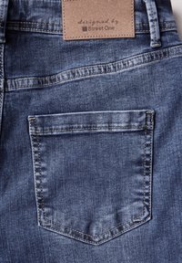 Jeans de mezclilla en un lavado azul oscuro, con un único bolsillo trasero con costuras visibles y una etiqueta de cuero marrón marcada con "diseñado por Street One."