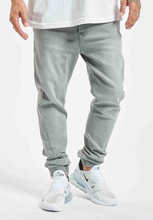 Homme portant un pantalon de jogging gris clair et des baskets blanches Nike Air Max 270, debout, les mains légèrement écartées.