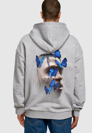 Sweat à capuche gris avec un graphique au dos de papillons bleus entourant un visage stylisé et le texte "LE PAPILLON." Design abstrait avec une texture douce.