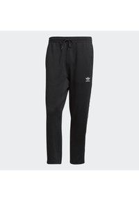 Pantalones de chándal negros hechos de material suave; cuentan con una cinturilla elástica con cordón, bolsillos laterales y un logo en el muslo izquierdo.