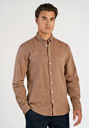 Camicia marrone a maniche lunghe con bottoni, realizzata in tessuto strutturato, con colletto appuntito e bottoni bianchi, indossata da un modello su uno sfondo semplice.