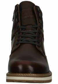 Bota de cuero marrón con ojales de metal, cordones negros y un cuello de tela texturizada. Suela blanca resistente con un detalle de costura visible.