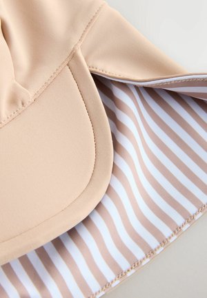 Beige kasket lavet af blødt stof med en buet skygge. Indersiden er foret med et stribet mønster i beige og hvid. Sømme detaljer er synlige.