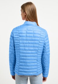 Blauwe gewatteerde jas met een kraag, horizontaal gestikte lijnen en elleboogpatches. Gemaakt van glad, lichtgewicht materiaal.