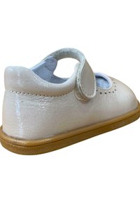 Zapato de charol blanco con punta redondeada, correa de Velcro, detalle perforado y suela de goma marrón. Estilo clásico Mary Jane.