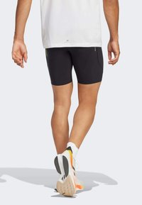 Schwarze Sportshorts mit einer enganliegenden Passform, kombiniert mit Schuhen in einem Farbschema aus Weiß, Orange und Schwarz.
