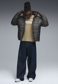 Puffjacka i mörkgrått med en vadderad design, tillsammans med en beige T-shirt med en logotyp, löst sittande mörk denimjeans och vita sneakers.