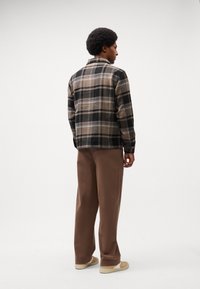 Plaid flannel shirt in beige, black, and blue with long sleeves, button closure, and a collar, paired with brown wide-leg trousers and sneakers.