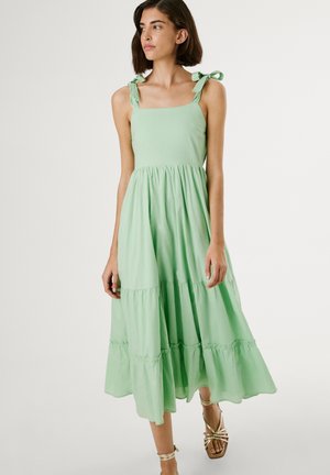 Light green cotton sundress with a square neckline, adjustable tie straps, and a tiered skirt. Features a flowing design and soft texture.
