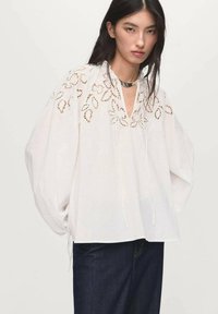 Hvid bluse med blomsterbroderi, lange puffærmer, v-hals og snore. Kombineret med blå denimbukser.