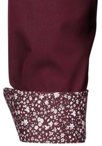 Burgunderfarbener Hemdmanschette mit floralem Muster in Weiß- und Rosatönen, versehen mit einem kontrastierenden Stoffbesatz mit kleinen Blumen.