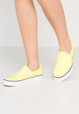 Gelbe Stoffschlupfschuhe mit einem weißen Innenfutter, schwarzem Akzent an der Sohle und flachem Design. Die Schuhe haben eine glatte Textur.