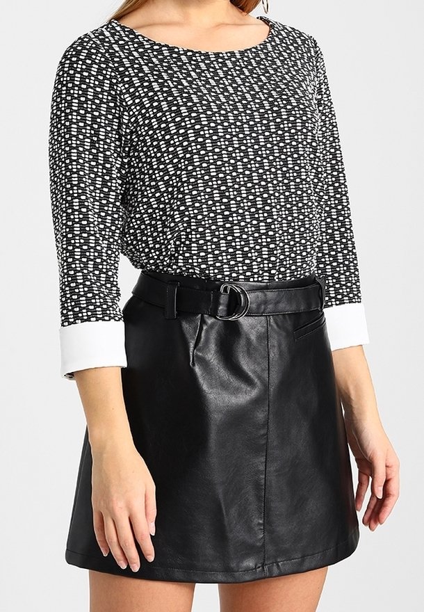 Svart och vit mönstrad topp med långa ärmar, kombinerad med en svart läderkjol i skaterstil som har bälte, slät textur och enkla detaljer.