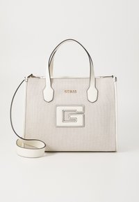 Vit texturerad handväska med svarta detaljer, som har en framträdande präglad logotyp, dubbla handtag och ett avtagbart axelband.