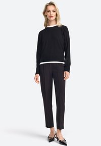 Zwarte trui met witte rand, gecombineerd met op maat gemaakte zwarte broek en puntige zwarte hakken. Gladde textuur, casual maar verfijnd design.