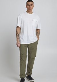 White short-sleeve t-shirt with a chest pocket paired with olive green cargo pants. Sneakers are black with a simple design.