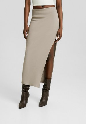 Beige gerippter Maxirock mit einem Seitenschlitz, kombiniert mit dunkelbraunen, lässigen Ankle Boots. Glatte Textur und figurnahes Design sind sichtbar.