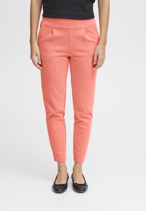 Pantalones de mezcla de poliéster color coral con corte entallado, que presentan pliegues frontales y bolsillos laterales. Combinados con zapatos planos negros.