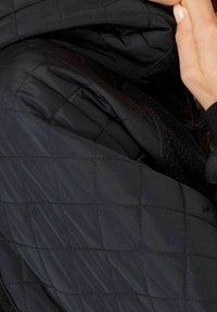 Giacca nera trapuntata con un esterno liscio e un rivestimento interno testurizzato. Presenta un colletto alto e una zip nascosta.