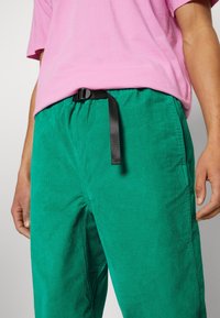 Gröna kordfläskbyxor med en texturerad yta, utrustade med ett svart justerbart bälte. Stylen har en avslappnad passform och sidofickor.