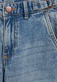 Hele sinise värvusega teksapüksid klassikalise viie taskuga disainiga. Vöökohal on messingist nupp ja õmbluste ääres oranž õmblusdetail.