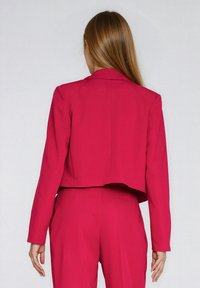 Krótka marynarka z żywego różowego materiału z klasycznym kołnierzem i długimi rękawami, charakteryzująca się gładką fakturą i dopasowanym krojem.