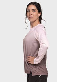 Long-sleeve athletic shirt in light pink and mauve gradation, featuring textured fabric, side slits, and a graphic detail on the sleeve.