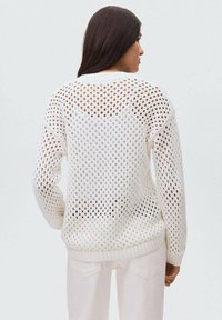 Weißer Strickpullover mit einem Lochmuster-Design, großen Löchern, gerippten Ärmelbündchen und geradem Schnitt. Die Ansicht zeigt die Rückseite.