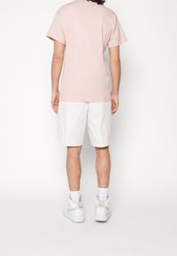 Světle růžové tričko s krátkým rukávem, spárované s bílými šortkami ke kolenům. Obuv: bílé sportovní tenisky s vysokým svrškem.