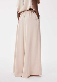 Wijde broeken van zacht, blush stof. Voorzien van een elastische tailleband, zijzakken en een gladde textuur voor comfort en bewegingsgemak.