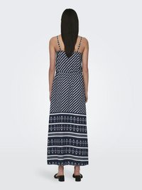 Mornarsko modra maksi obleka z belimi diagonálnimi črtami in geometrijskimi vzorci na robu. Obleka ima tanko naramnice in poudarjen pas.