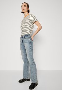 Csíkos póló narancssárga nyakkal, világoskék harangszárú farmernadrággal. Fekete bokacsizma zárja le a szettet. Texturált denim szövet.