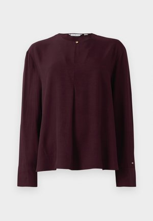 Blouse à manches longues de couleur bourgogne foncé avec un col rond, un pli avant et une fermeture par un bouton doré au niveau du cou.