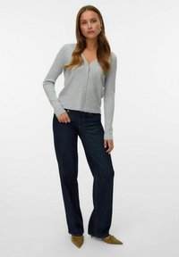 Grijze geribbelde cardigan met een V-hals, knoopsluiting en lange mouwen. Gecombineerd met donkerblauwe rechte jeans en lichtgroene spitse schoenen.