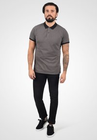 Polo gris avec un motif texturé, col noir et bordures de manches noires. Associé à un jean noir et des baskets noires.
