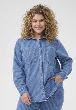 Chemise en denim bleu à boutons avec des rayures verticales blanches, deux poches poitrine et un ourlet arrondi, dotée de manches longues et d'une coupe décontractée.