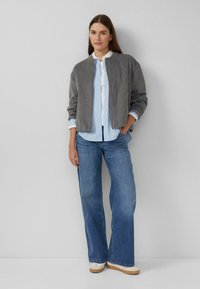 Szara kurtka typu bomber z mieszanki wełny, w połączeniu z jasnoniebieską, paskowaną koszulą na guziki, szerokimi niebieskimi dżinsami oraz beżowymi butami na platformie.