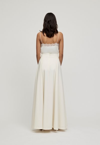 Jupe maxi en satin blanc avec une taille ajustée et une silhouette fluide, associée à un caraco délicat à dentelle. Texture lisse, design minimaliste.