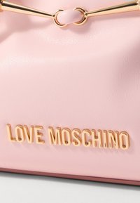 Różowa torebka z ekoskóry z akcentem w złotym odcieniu oraz wytłoczonym logo "LOVE MOSCHINO" z przodu, o gładkiej fakturze.