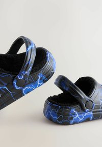 Sabots à motifs noir et bleu avec un intérieur doux, un design à dos ouvert et une sangle ajustable. Surface texturée avec des accents bleus évoquant des éclairs.