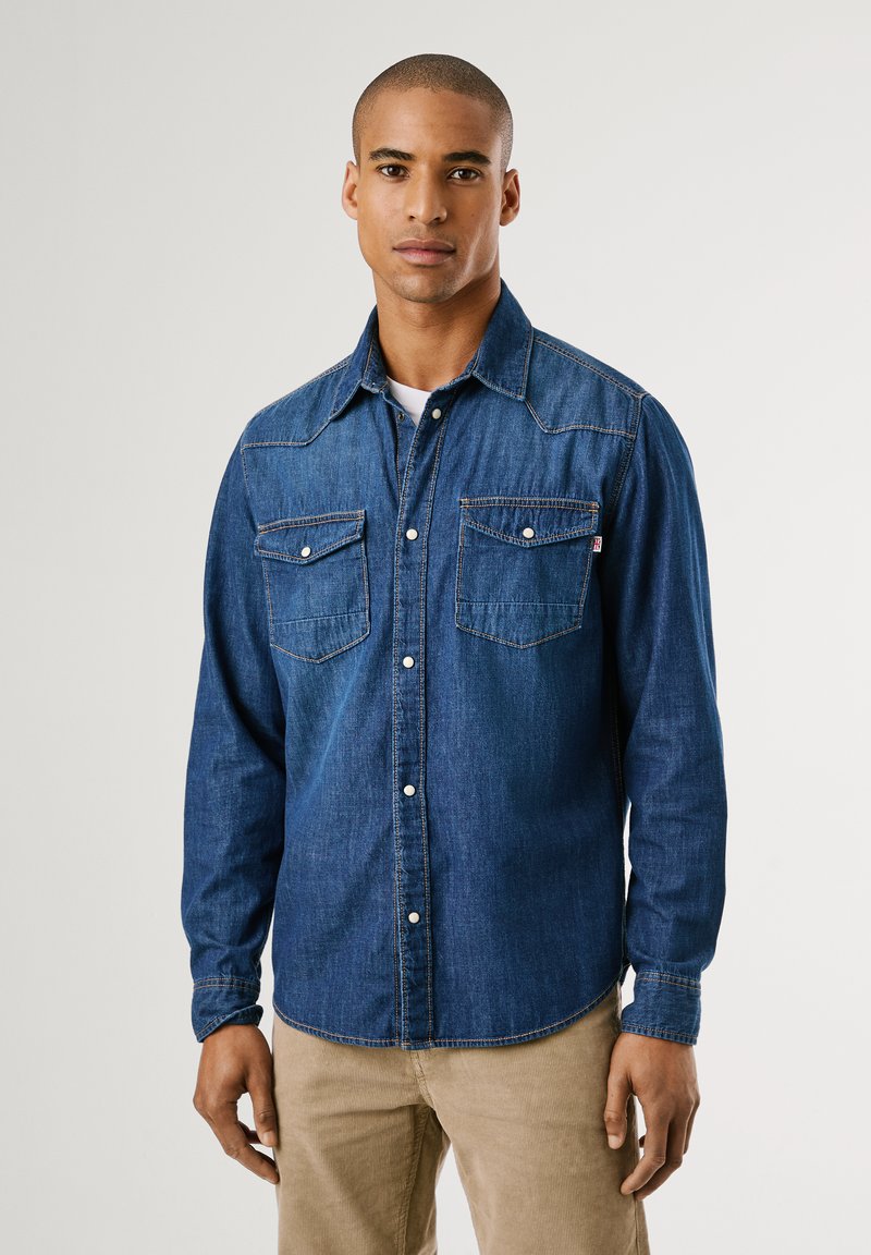 Donkerblauwe denim shirt met een klassiek ontwerp, puntige kraag, twee borstzakken en witte knoopsluitingen. Textuurstof met zichtbare stiksels.