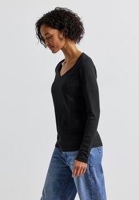 Schwarzes Langarm-V-Ausschnitt-Top aus weichem Material, kombiniert mit hellblauen Jeans im relaxed Fit und abgerundetem Saum.